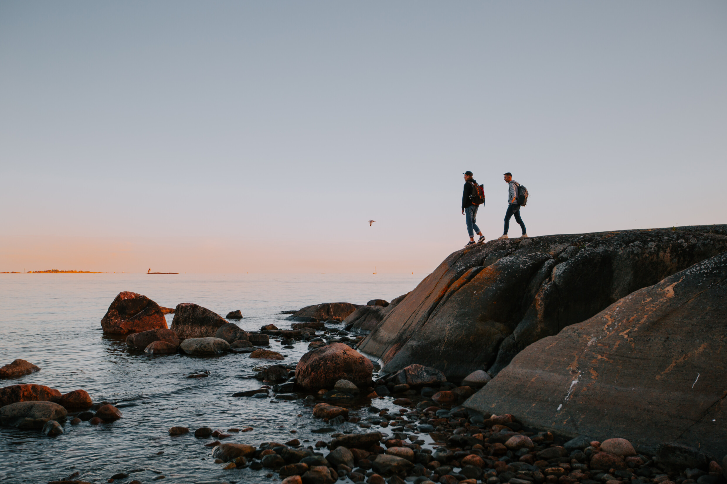 Kaksi retkeilijää seisoo Kalliolla ja katsovat merelle auringon laskun jälkeen.